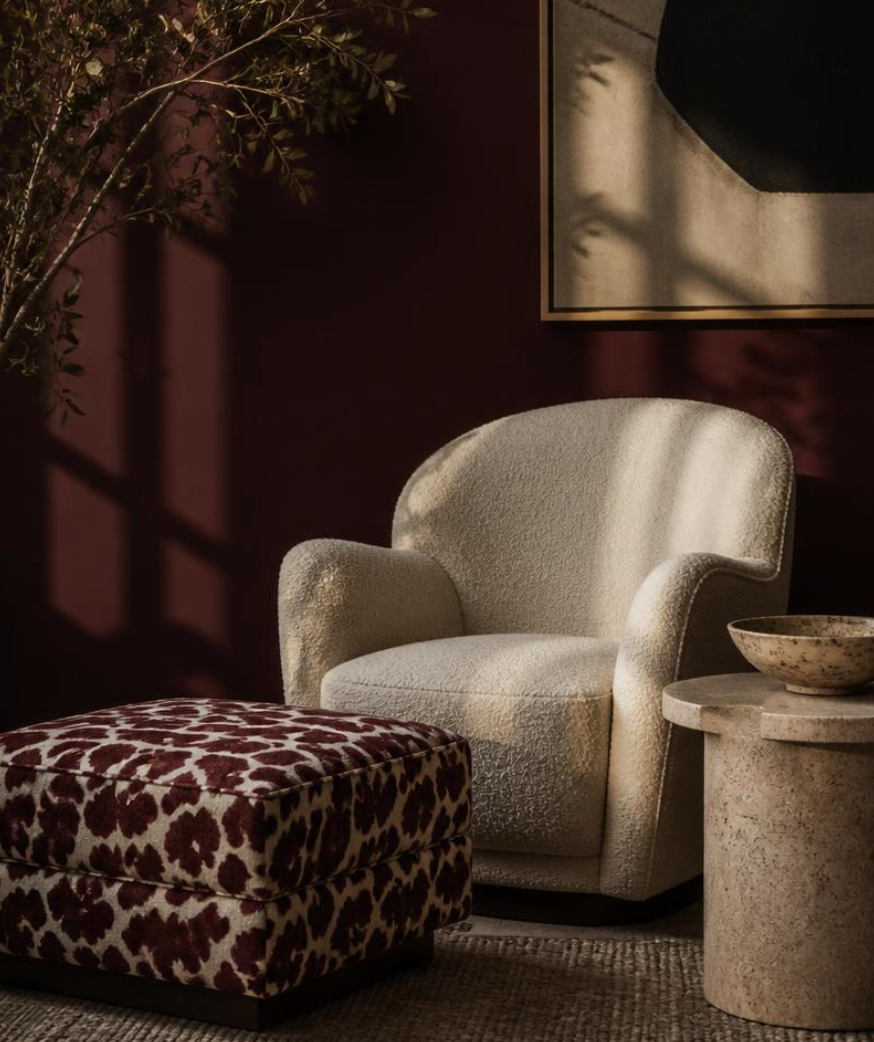 A square upholstered ottoman with a bold red and off-white cow-print pattern and four tapered light wood legs, set against a solid dark red background.