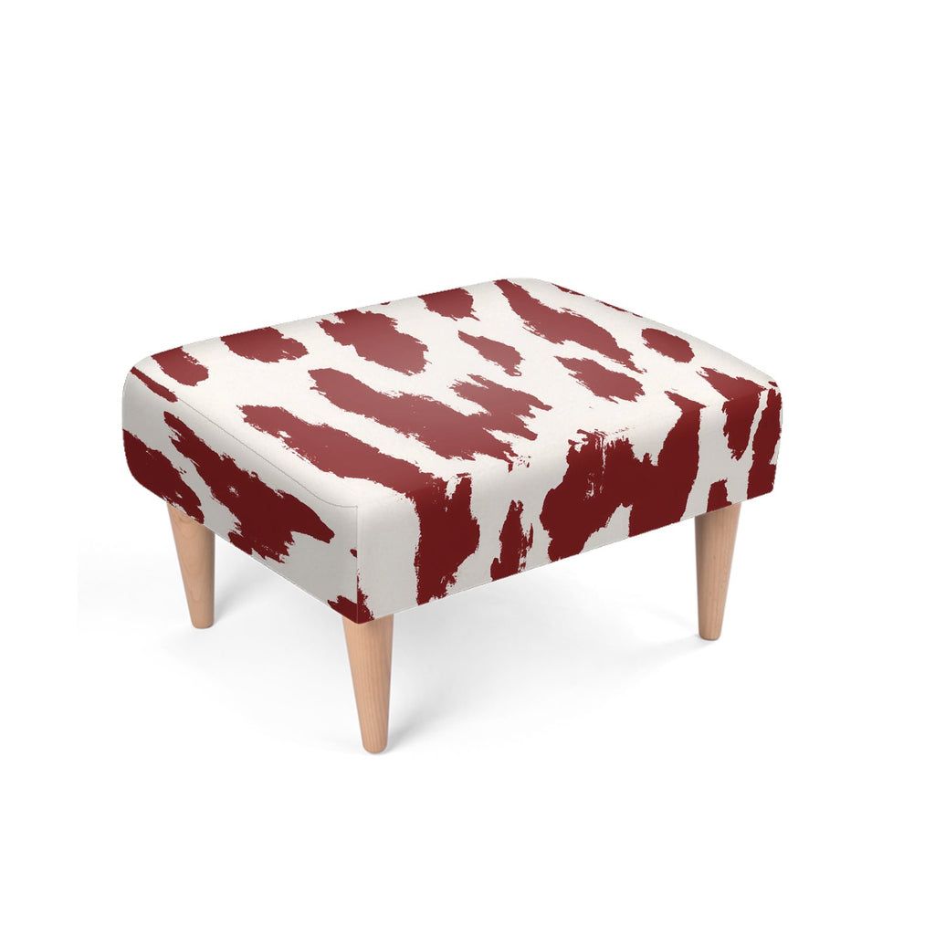 A square upholstered ottoman with a cream fabric covered in bold dark red abstract brushstroke pattern, supported by four tapered light wood legs, shown on a white background.